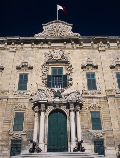 MALTA, Valletta, Auberge de Castille et Leon. Decorative baroque facade with steps leading to green doorway flanked by pillars and cannons with the Maltese flag flying from roof. Official residence of the Prime Minister