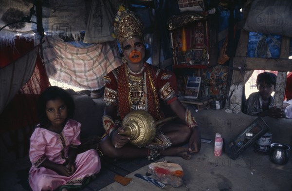 INDIA, Gujarat, Bhavnagar, Man in his shanty house dressed up as the Hindu deity Hanuman.  Child looking in through open window and little girl sitting beside him.