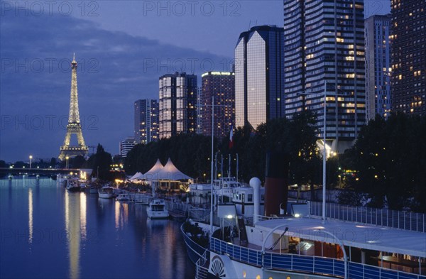 FRANCE, Ile de France, Paris, Modern high rise buildings and the Eiffel Tower from the banks of the River Seine illuminated at dusk.