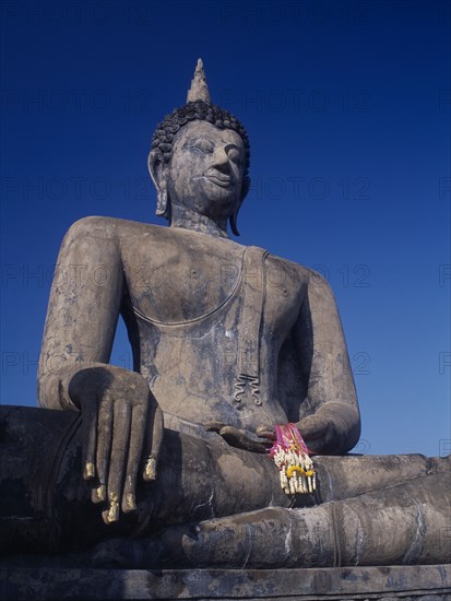 THAILAND, North, Sukhothai Province, Wat Mahathat. Seated Buddha statue holding pink ribbon flower garlands