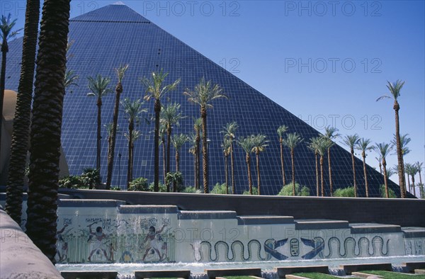 USA, Nevada, Las Vegas, The Luxor Hotel exterior with replica pyramid and hieroglyphics.  Water feature and line of palm trees in the foreground.