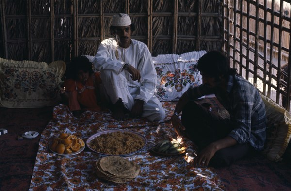 OMAN, Food, Two men and girl sitting with a meal served in communal dishes in front of them.