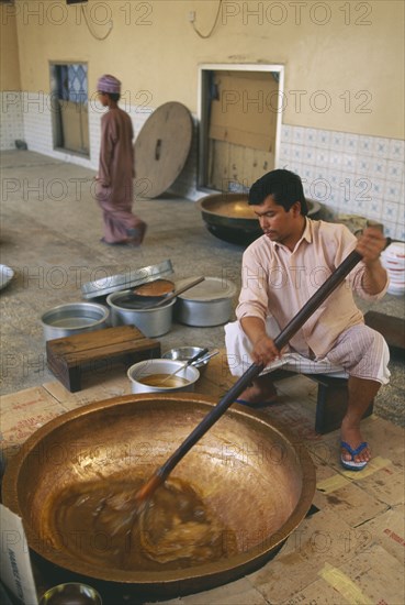 OMAN, Food , Man stirring in butter to Halva mixture