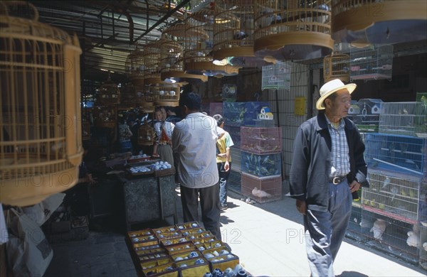 CHINA, Yunnan , Kunming, A man wearing a hat walking through a alley way in a Bird and Flower market surrounded by bird cages.