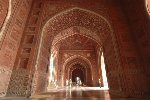 INDIA, Uttar Pradesh, Agra, "Taj Mahal, with an 9nterior view of the elaborate red sandstone hallway and arches of the western mosque with people walking through"