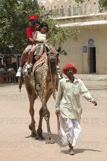 INDIA, Rajasthan, Jaipur, Man leading camel with three children riding on its back