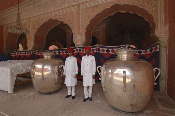 INDIA, Rajasthan, Jaipur, At the Jaipur city palace two guards dressed in white with red turbans standing between two massive silver urns used by the Maharaja Sawai Mansingh II to carry holy water from the Ganges