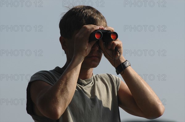 ROMANIA, Tulcea, Danube Delta Biosphere Reserve, Male tourist with binoculars with scenery reflected in orange in his binoculars
