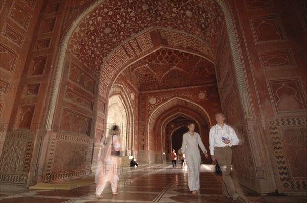 INDIA, Uttar Pradesh, Agra, "Taj Mahal, with an 9nterior view of the elaborate red sandstone hallway and arches of the western mosque with people walking through"