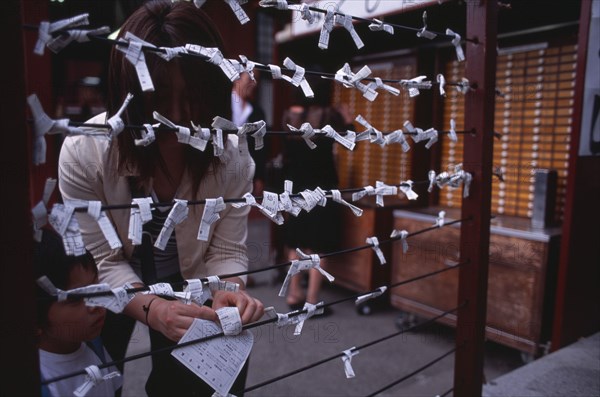 JAPAN, Honshu, Tokyo, Asakusa. People tying Omikuji or Fortune papers at Senso Ji Temple