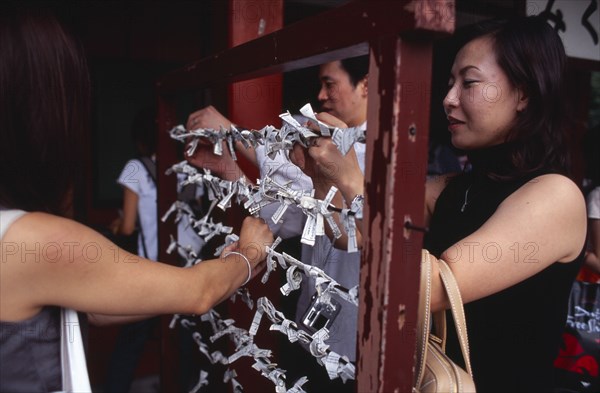 JAPAN, Honshu, Tokyo, Asakusa. People tying Omikuji or Fortune papers at Senso Ji Temple