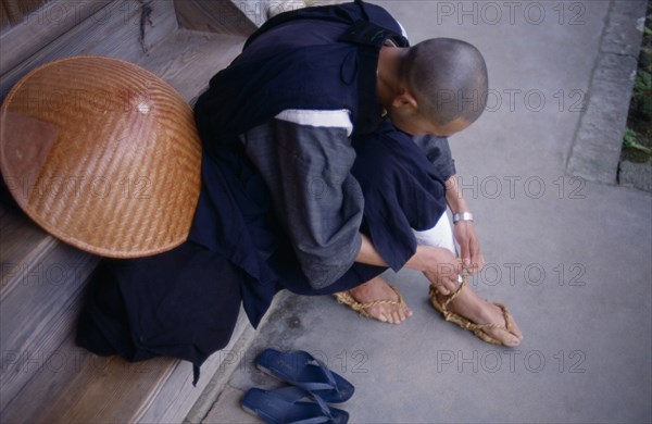 JAPAN, People, Bukokuji Monastery with Zen Buddhist monk tying up thong sandal made of rope.