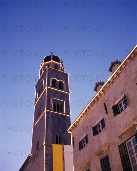 CROATIA, Dalmatia, Dubrovnik, Angled view looking up at the Francisan Monastery tower illuminated at dusk