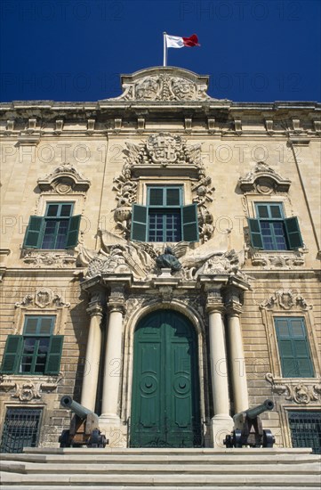 MALTA, Valletta, Auberge de Castille et Leon. Decorative baroque facade with steps leading to green doorway flanked by pillars and cannons with the Maltese flag flying from roof. Official residence of the Prime Minister