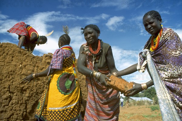 UGANDA, Industry, Construction, Brightly dressed Karamojong women making bricks. Blue sky behind.