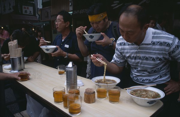 JAPAN, Honshu, Tokyo, Tsukiji Fish Market. People eating with chopsticks at noodle stall