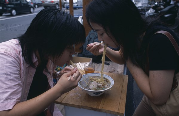 JAPAN, Honshu, Tokyo, Tsukiji Fish Market. Two girls sharing a bowl of noodles at a street stall