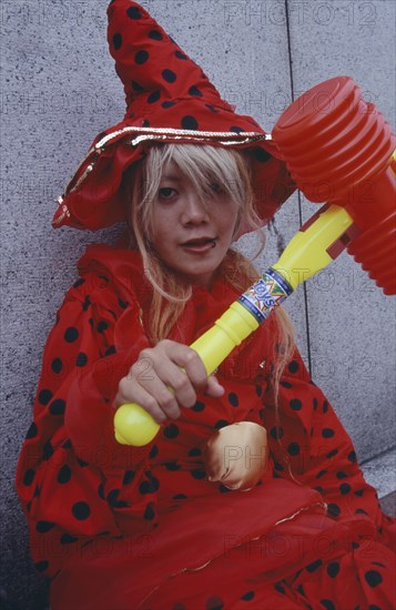 JAPAN, Honshu, Tokyo, Harajuku District. Portrait of young teenage girl wearing a red and black spotted outfit holding a toy hammer