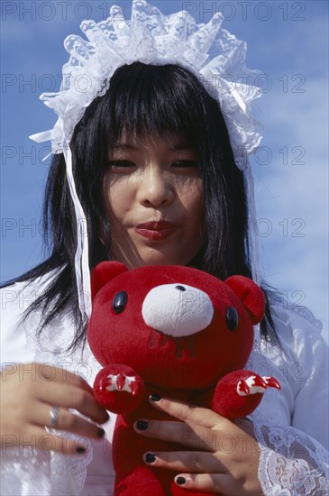 JAPAN, Honshu, Tokyo, Harajuku District. Portrait of a teenage girl wearing white lace dress holding a red teddy bear