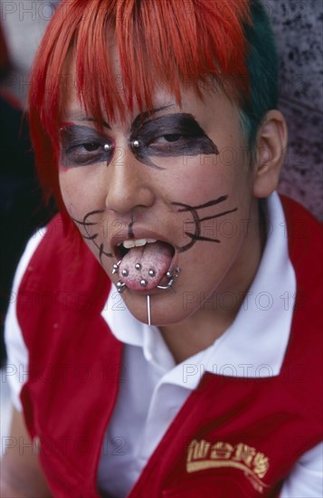 JAPAN, Honshu, Tokyo, Harajuku District. Portrait of a teenage girl wearing cat whisker makeup with several tongue and facial piercings