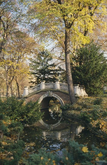 FRANCE, Ile de France, Paris, Parc Monceau created by landscape designer Louis Carmontelle.  Arched bridge over stream surrounded by trees.
