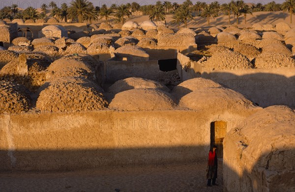 20032915 ALGERIA  Architecture Typical mud architecture with woman wearing red standing in the foreground.