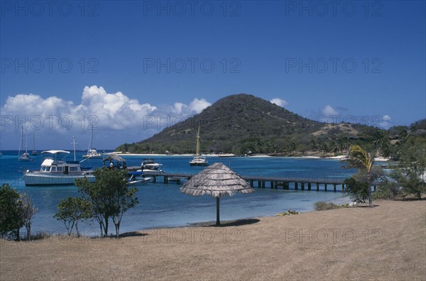 GRENADINES, Petit St Vincent, Golden beach with umbrellas and hills in the distance