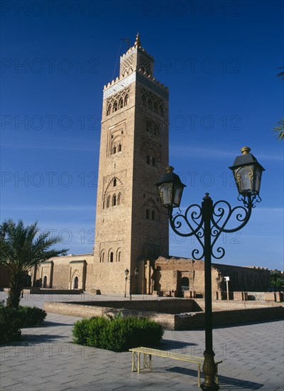 MOROCCO, Marrakech, Koutoubia Mosque tower seen from pavement with blue sky behind and street lamps in foreground