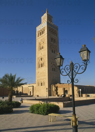 MOROCCO, Marrakech, Koutoubia Mosque tower seen from pavement with blue sky behind and street lamps in foreground