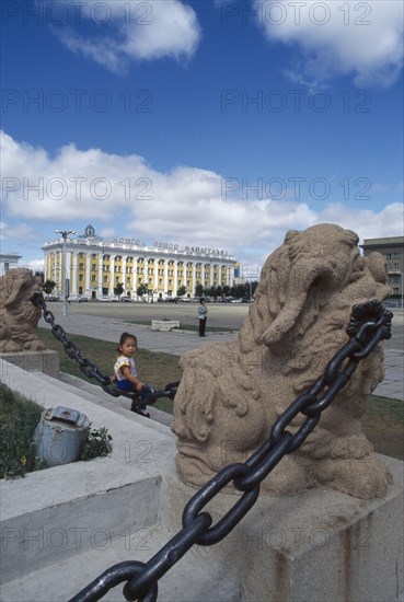 MONGOLIA, Ulan Bator, Sukhbaatar square with small girl sitting on chainlink fence around steps in foreground.