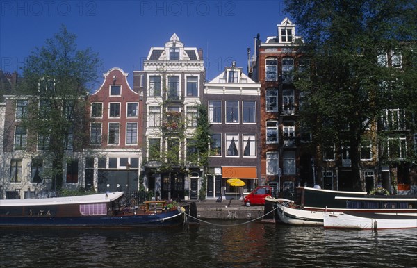 HOLLAND, Noord, Amsterdam, Moored barge on the side of the Oude Schans canal lined with traditional architecture