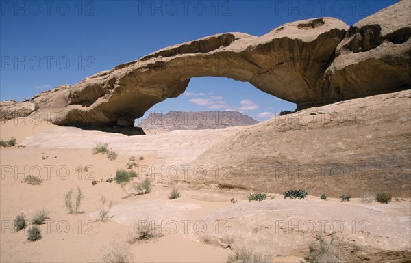 JORDAN, Wadi Rum Desert, Rock formation in the form of natural arch framing view to distant flat topped rock