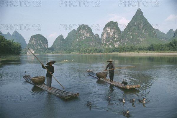 CHINA, Guilin, River Li, Cormorant fishermen on narrow rafts with birds swimming ahead.