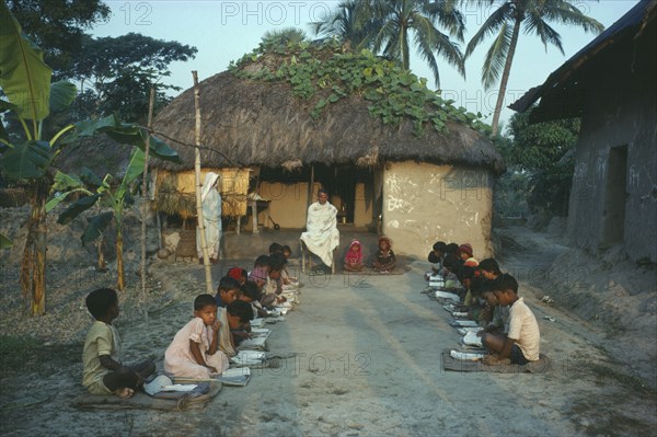 INDIA, West Bengal, Pathasala, Outdoor informal school. Pupils seated in two lines facing each other with teacher at head.
