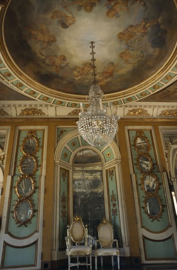 PORTUGAL, Near Lisbon, Palacio Nacional de Queluz interior. Sala dos Exbaixadores with throne chairs and detail of hanging chandelier and ceiling frescos.