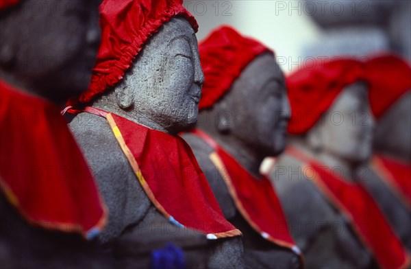JAPAN, Honshu, Kamakura, View along row of Jizo statues dressed in red bibs by bereaved mothers and other sufferers