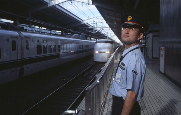 JAPAN, Honshu, Kyoto, Bullet train aka Shinkansen pulling into the station platform with train guard standing in the foreground