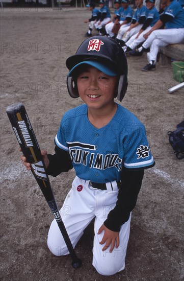 JAPAN, Honshu, Tono, Young boy kneeling on the grass wearing a Baseball kit holding a bat