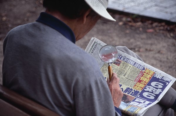 JAPAN, Honshu, Hiroshima, View over the shoulder of a man reading the newspaper with a magnifying glass