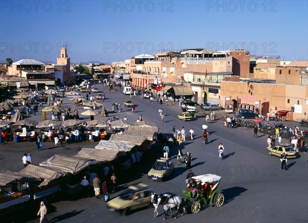 MOROCCO, Marrakech, Djemaa El Fina Square. View over busy market square with people at stalls and buildings behind.