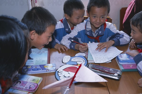 CHINA, Yunnan Province, Children in their classroom working in groups with various school materials on the table in front of them.