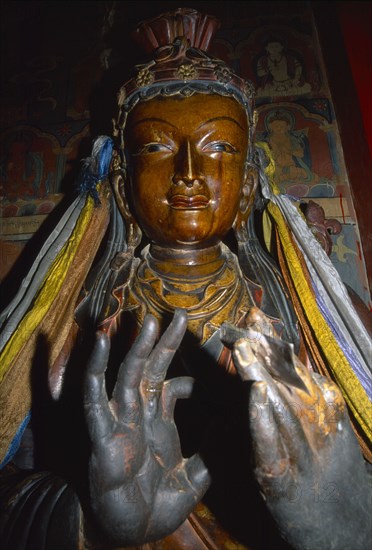 TIBET, Gyantse, Interior of the Assembly Hall with a figure of a Buddha with hands in the foreground and paintings on the wall behind.