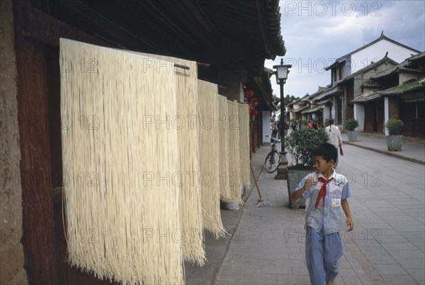CHINA, Yunnan, Dali., Weishan. Racks of noodles hanging out to dry in street with a boy walking past on pavement.