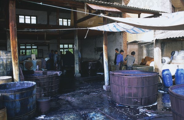 CHINA, Yunnan , Dali, Weishan. Batik factory with men working around  vats of dye under ornings.