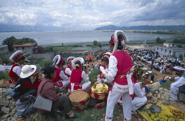 CHINA, Yunnan, Dali, Group of Bai ethnic minority girls in traditonal costume above a market with the sea in the distance.