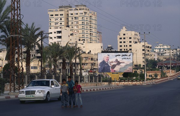 GAZA STRIP, Gaza City, Children on quiet road with billboard of Yasser Arafat and city buildings behind.
