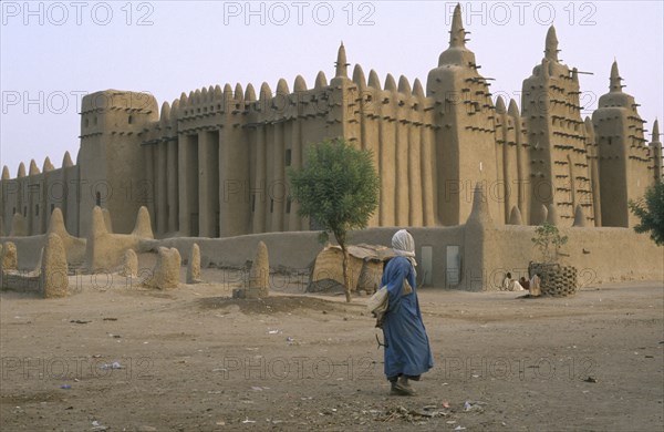 MALI, Djenne, Exterior of mud mosque with man crossing barren ground in the foreground.