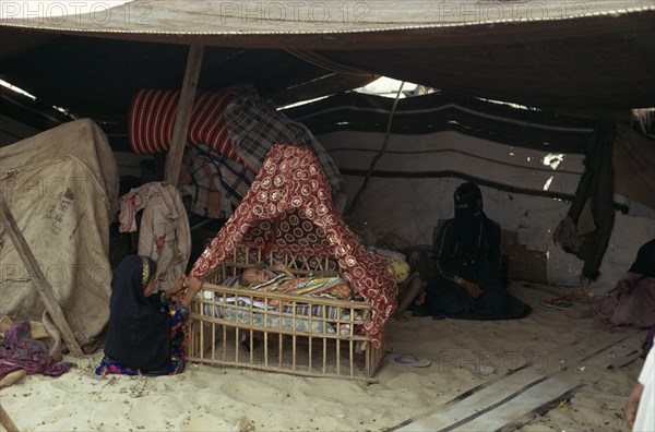 MIDDLE EAST, People, Bedouin desert encampment.  Woman and children inside tent with baby in traditional cradle
