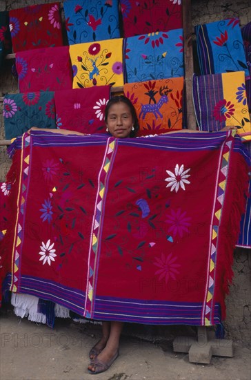 MEXICO, Chiapas, Zinacantan, Young girl holding up brightly coloured embroidered local cloth for sale.