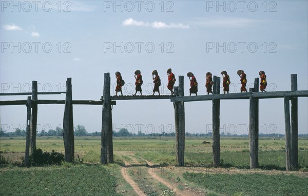 MYANMAR, Amarapura Bridge, Line of monks crossing two hundred and fifty year old bridge over flood plain near Mandalay.